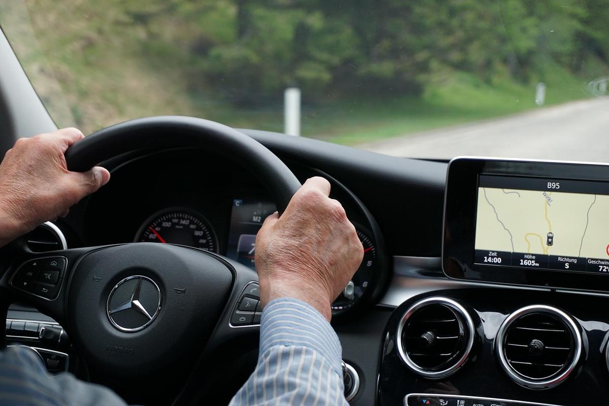 Un conducteur tient le volant d'une Mercedes, le GPS indique la route