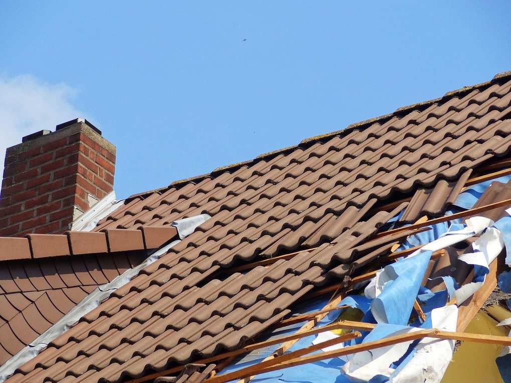 Toit endommagé avec charpente visible et échafaudage en bois sous un ciel bleu