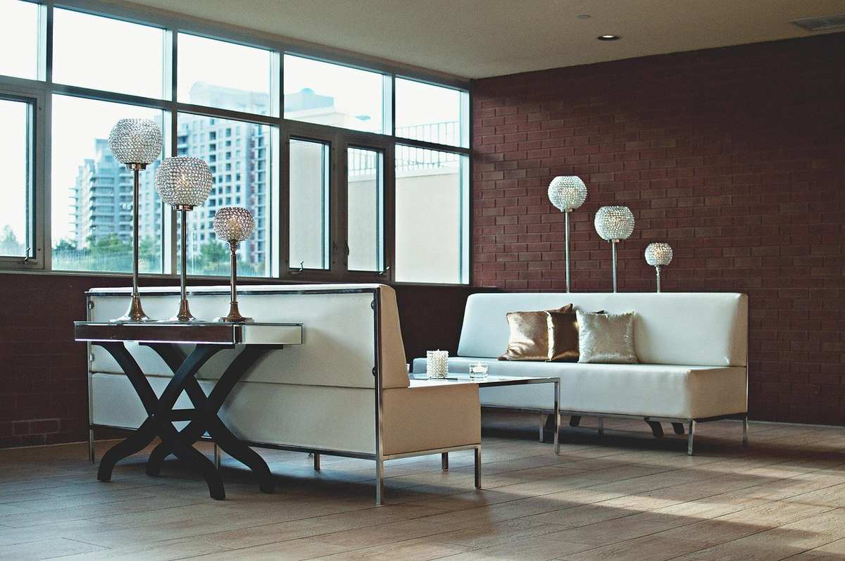 Salle de réunion avec canapés, tables, lampes, et vue sur des immeubles par des fenêtres
