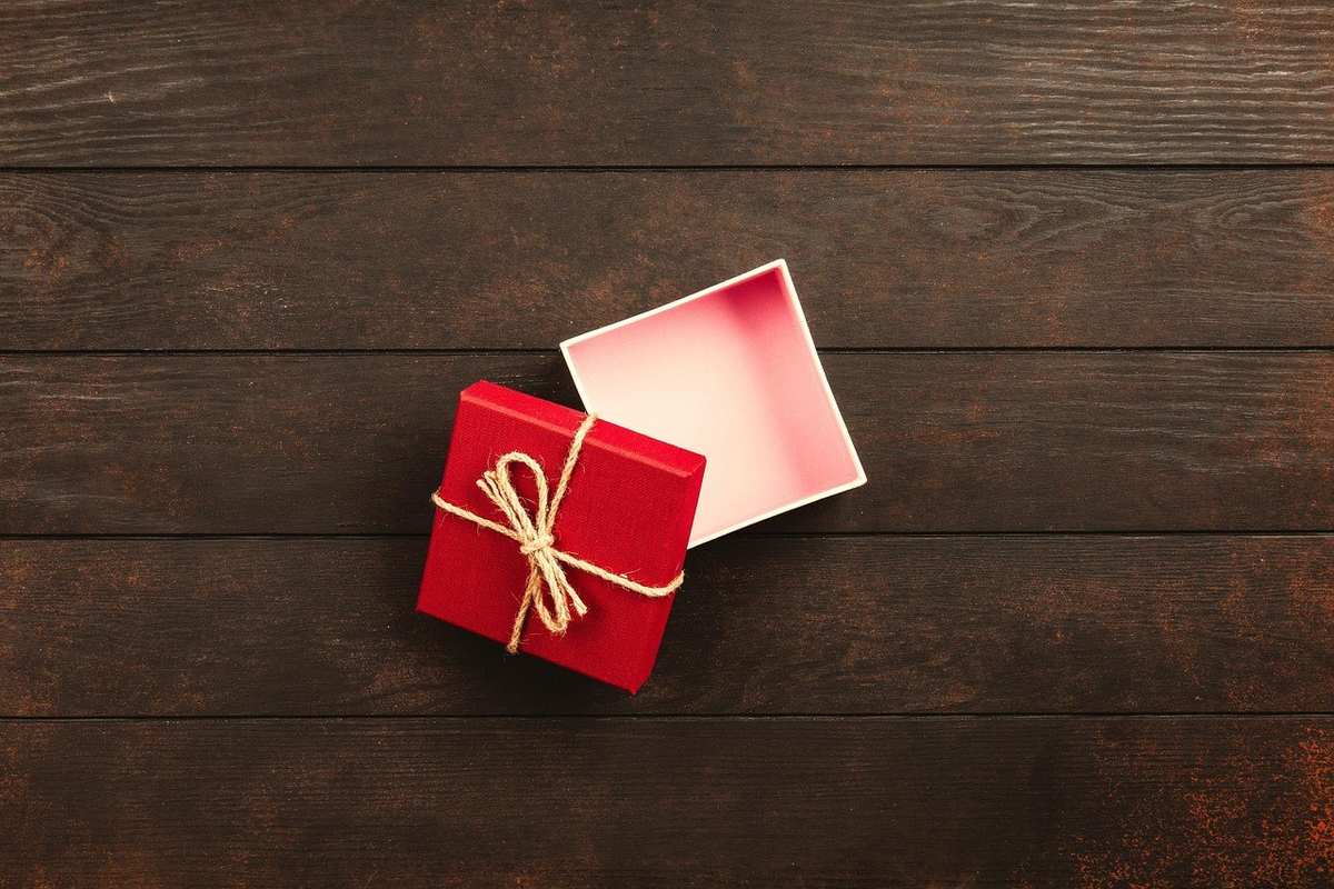 Cadeau rouge noué avec une ficelle sur une table en bois. Boîte blanche à côté