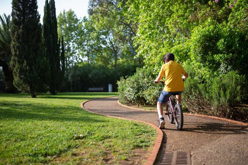 Enfant à vélo sur un chemin de parc, verdure et ciel en arrière-plan