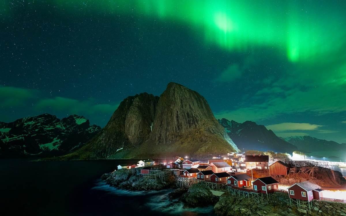 Village illuminé sous les aurores boréales, montagnes et ciel étoilé