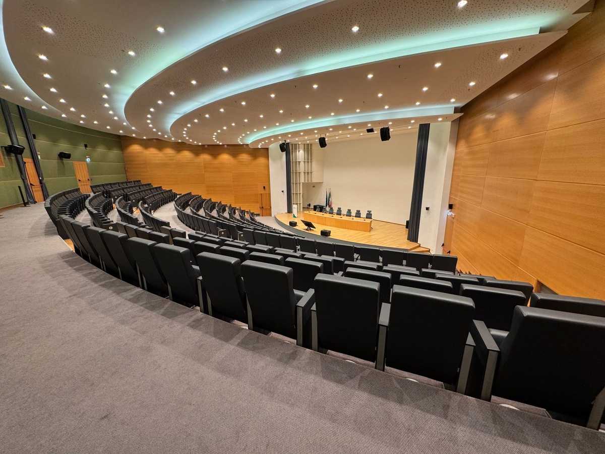 Salle de conférence avec amphithéâtre, sièges noirs, scène, éclairage, murs en bois Salle de conférence avec amphithéâtre, sièges noirs, scène, éclairage, murs en bois