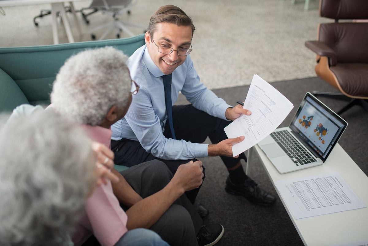 Professionnel partage un document avec deux personnes âgées dans un salon Professionnel partage un document avec deux personnes âgées dans un salon