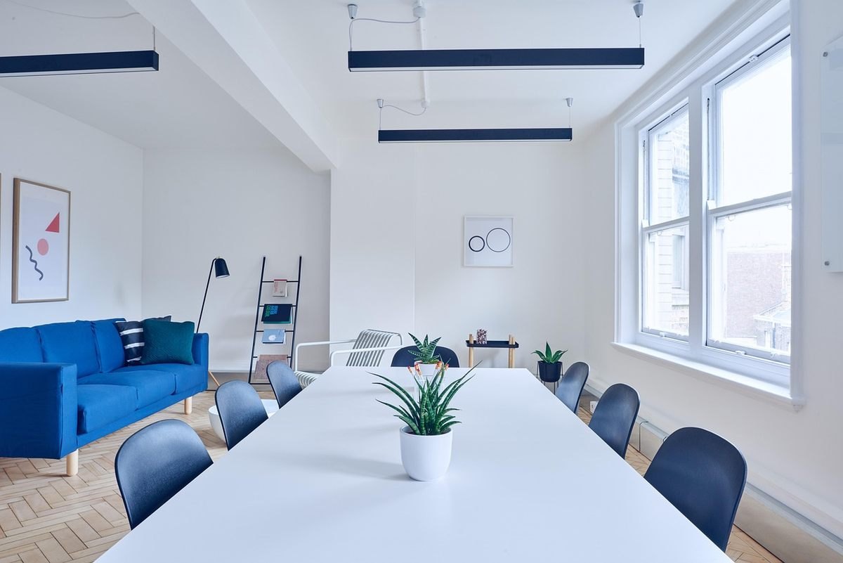 Salle de réunion avec table blanche, chaises bleues, canapé bleu, plantes, fenêtres, éclairage suspendu Salle de réunion avec table blanche, chaises bleues, canapé bleu, plantes, fenêtres, éclairage suspendu