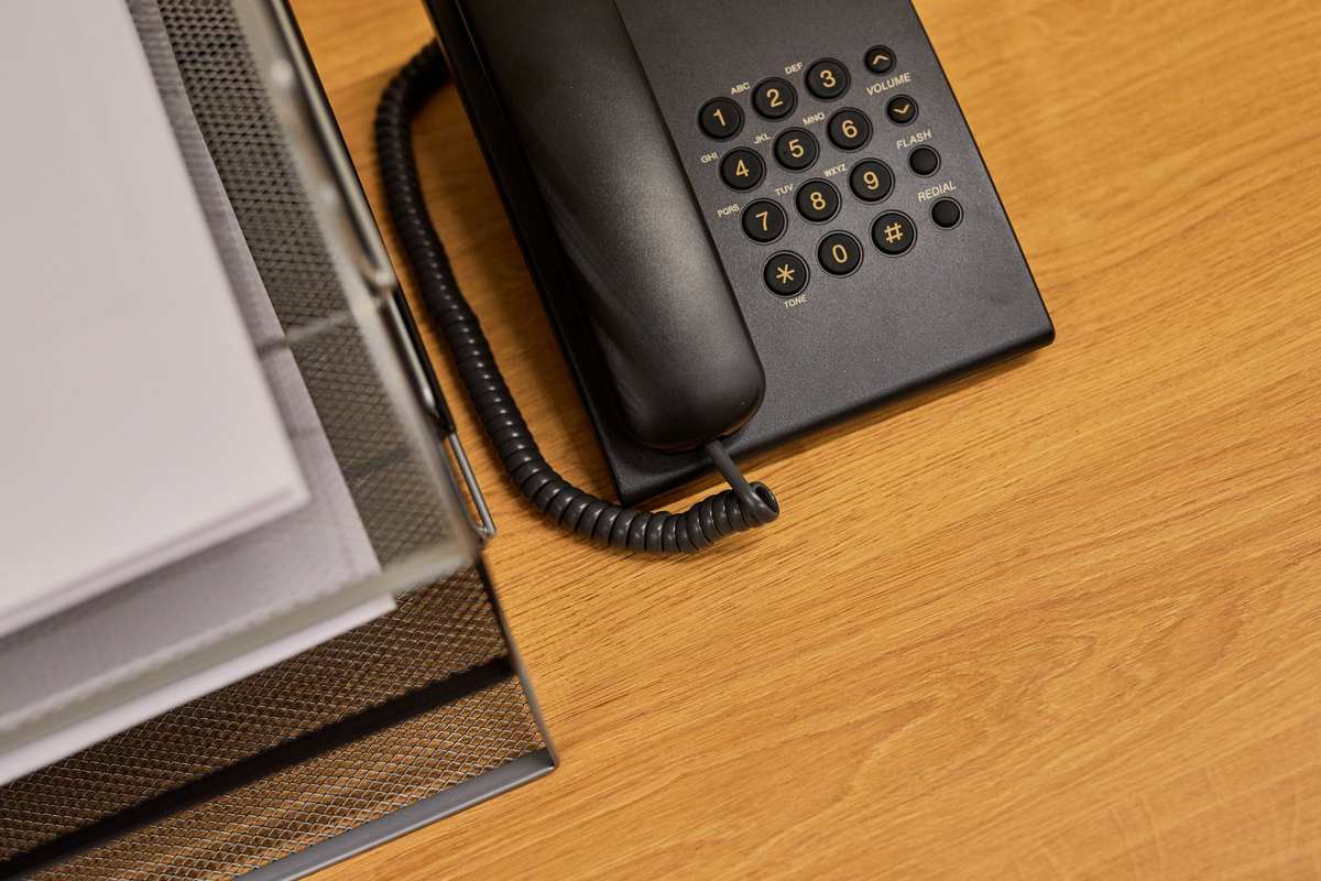 Un téléphone fixe posé sur un bureau en bois à côté d'un classeur