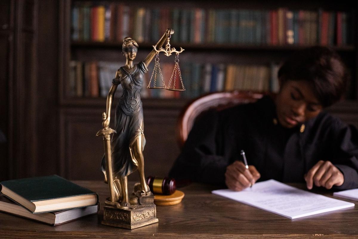 Statue de la justice, gavel, livres, personne écrivant dans une bibliothèque