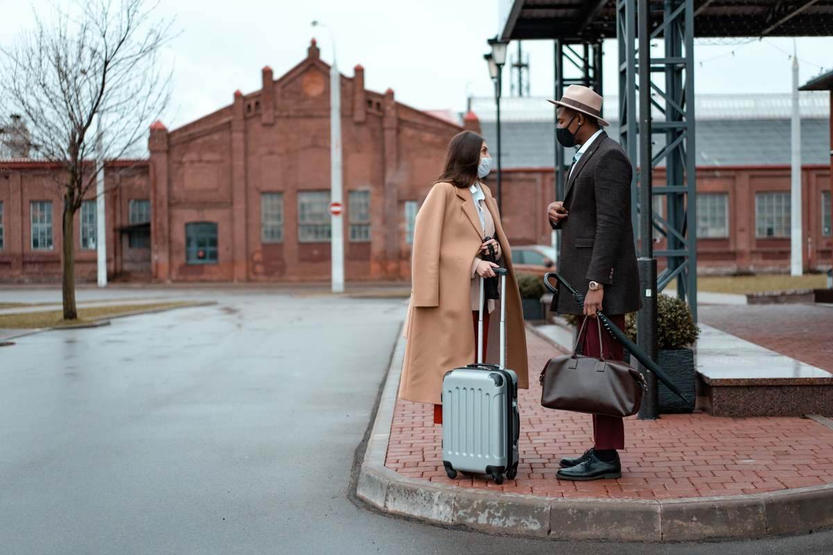 Deux voyageurs avec valise cabine et bagages devant architecture rouge urbaine